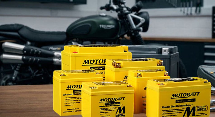 A modern AGM motorcycle battery on a workshop bench with professional tools and a blurred motorcycle in the background, lit with clean studio lighting.