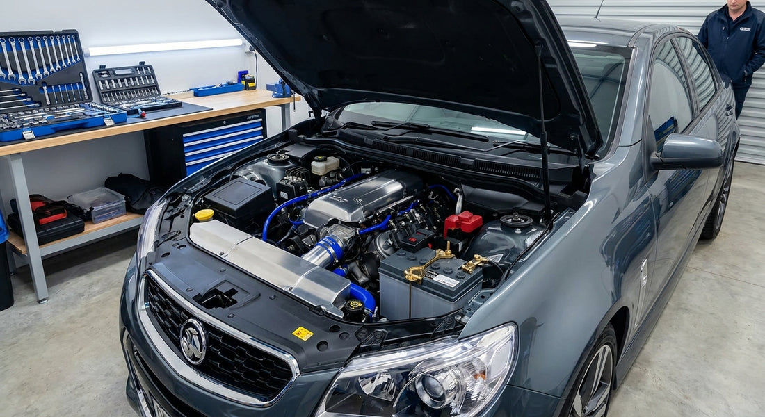 A modern car with its bonnet raised in a clean garage workshop, showing a newly installed car battery in the engine bay with tools neatly arranged nearby.