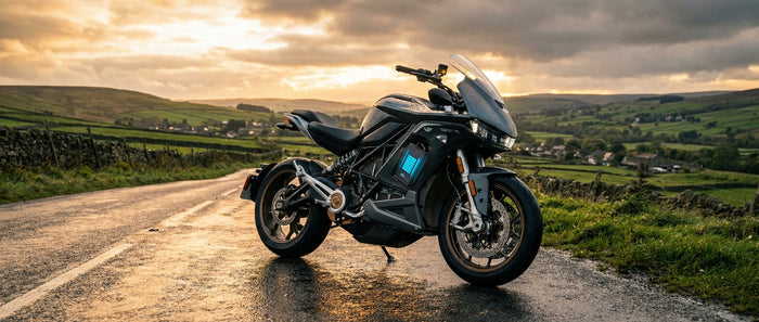 A modern motorcycle parked on a wet UK country road at golden hour with its battery compartment subtly visible, set against rolling green hills and a dramatic sky.