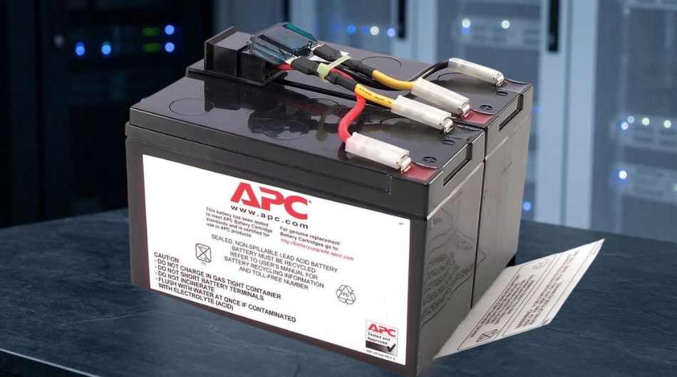 A UPS replacement battery cartridge photographed in dramatic studio lighting against a blurred server room background, conveying technical reliability and power continuity.