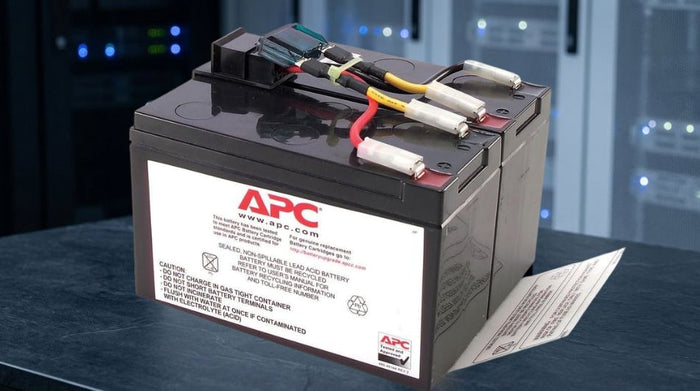A UPS replacement battery cartridge photographed in dramatic studio lighting against a blurred server room background, conveying technical reliability and power continuity.